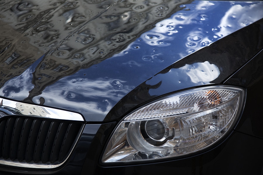 Close-up image of the damaged, dented surface of a black sedan and its driver's side headlight.