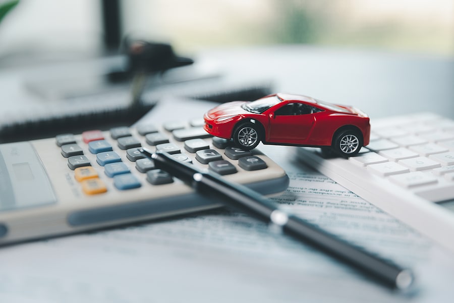 Toy red car on calculator and paperwork, symbolizing auto insurance claims and vehicle repair costs.
