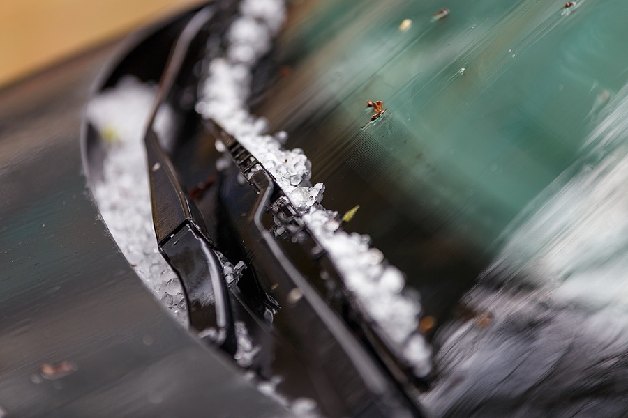 Close-up of small hailstones on a black car hood after a summer storm, with selective focus and natural daylight.